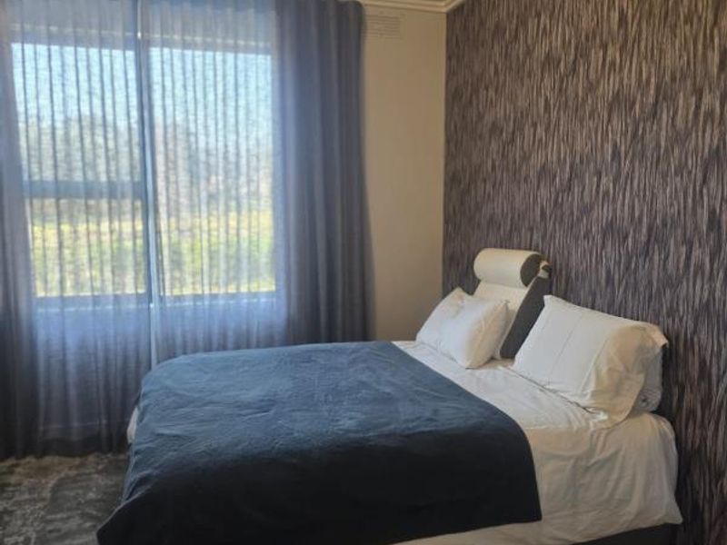 A well-lit bedroom featuring a textured feature wall, large window with curtains, and timber flooring.