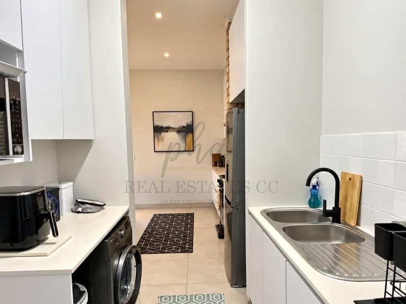 A modern, functional scullery featuring clean white cabinetry, stone countertops, a double stainless steel sink with a black tap, and tiled splashbacks.