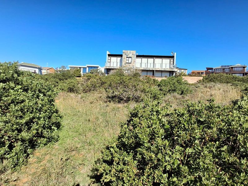 A view of a vacant residential plot featuring natural vegetation and a sloped landscape with neighboring properties visible in the background.