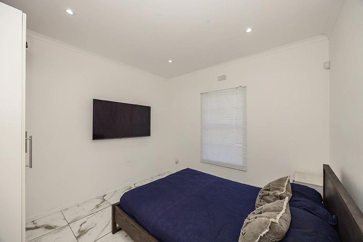 A bright bedroom featuring modern white marble-look floor tiles, recessed downlighting, and a built-in wardrobe.