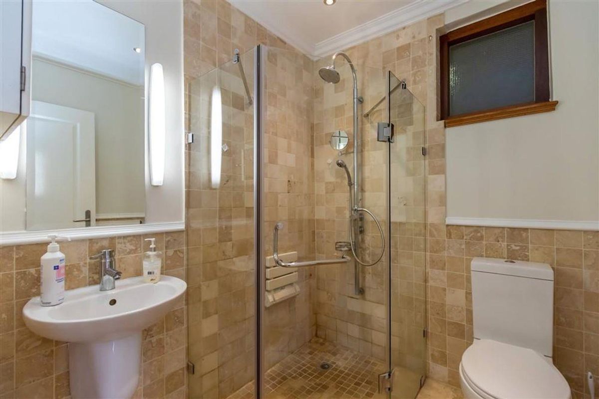 A well-maintained bathroom featuring a glass-enclosed shower with a built-in seat, a pedestal basin, and neutral stone-style wall tiling.