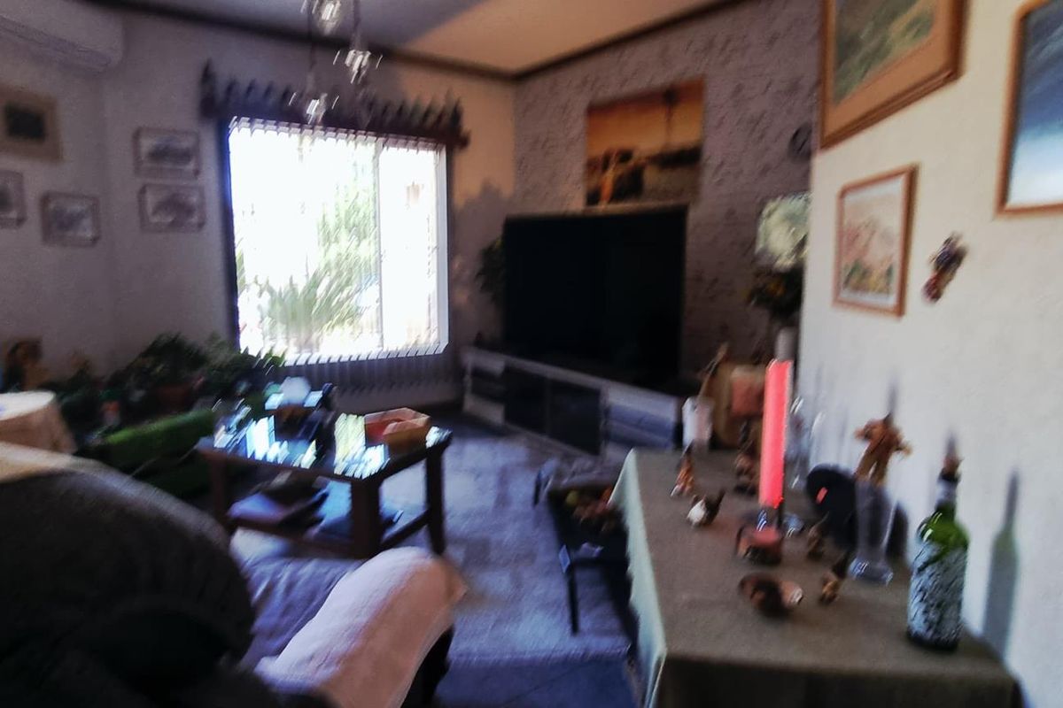 A living room featuring a split-system air conditioner and large windows with security bars, providing natural light to the space.