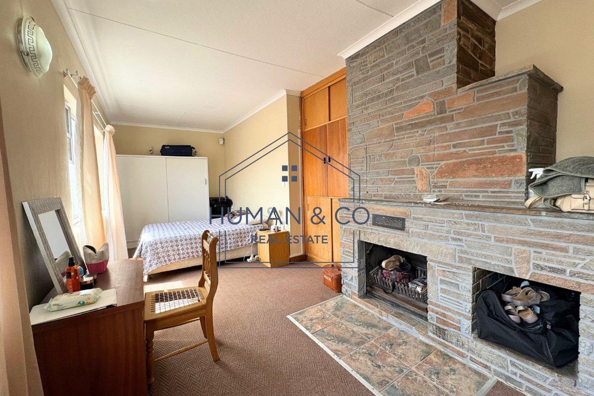 A bedroom featuring a prominent stone-clad fireplace, built-in wooden cabinetry, and carpeted flooring.