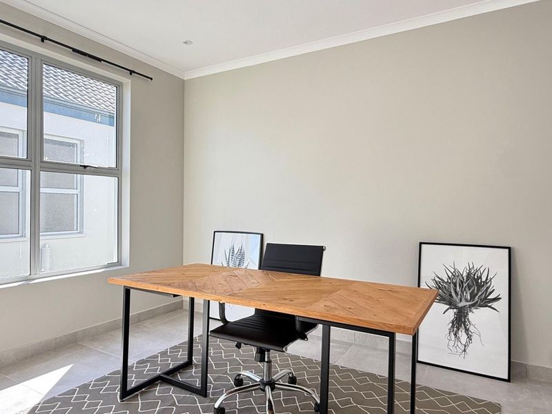 A bright and neutral home office featuring tiled flooring, large aluminium-framed windows, and recessed downlighting, offering a clean and functional workspace.