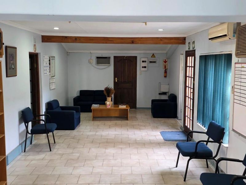 A functional office reception or waiting area featuring tiled flooring, recessed lighting, an exposed timber beam, and wall-mounted air conditioning.