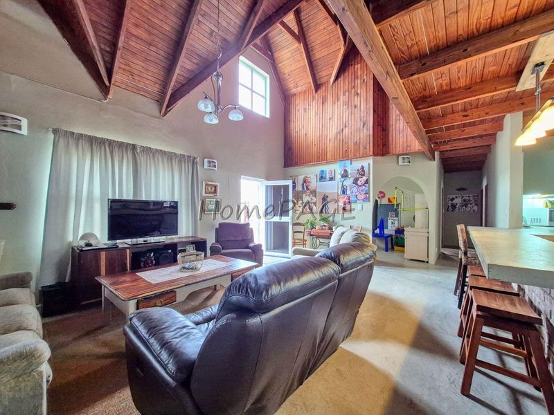 Spacious open-plan living area featuring a high vaulted timber ceiling with exposed beams, a breakfast bar, and an arched transition to adjacent spaces.