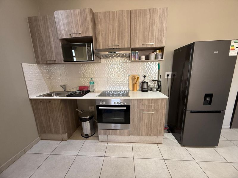 Compact modern kitchen featuring wood-grain cabinetry, integrated appliances including an oven and hob, and a decorative tiled backsplash.