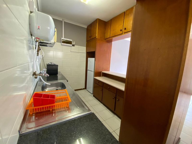 A functional kitchen featuring wooden cabinetry, tiled splashbacks, and a stainless steel sink, offering a practical layout with potential for modern updates.