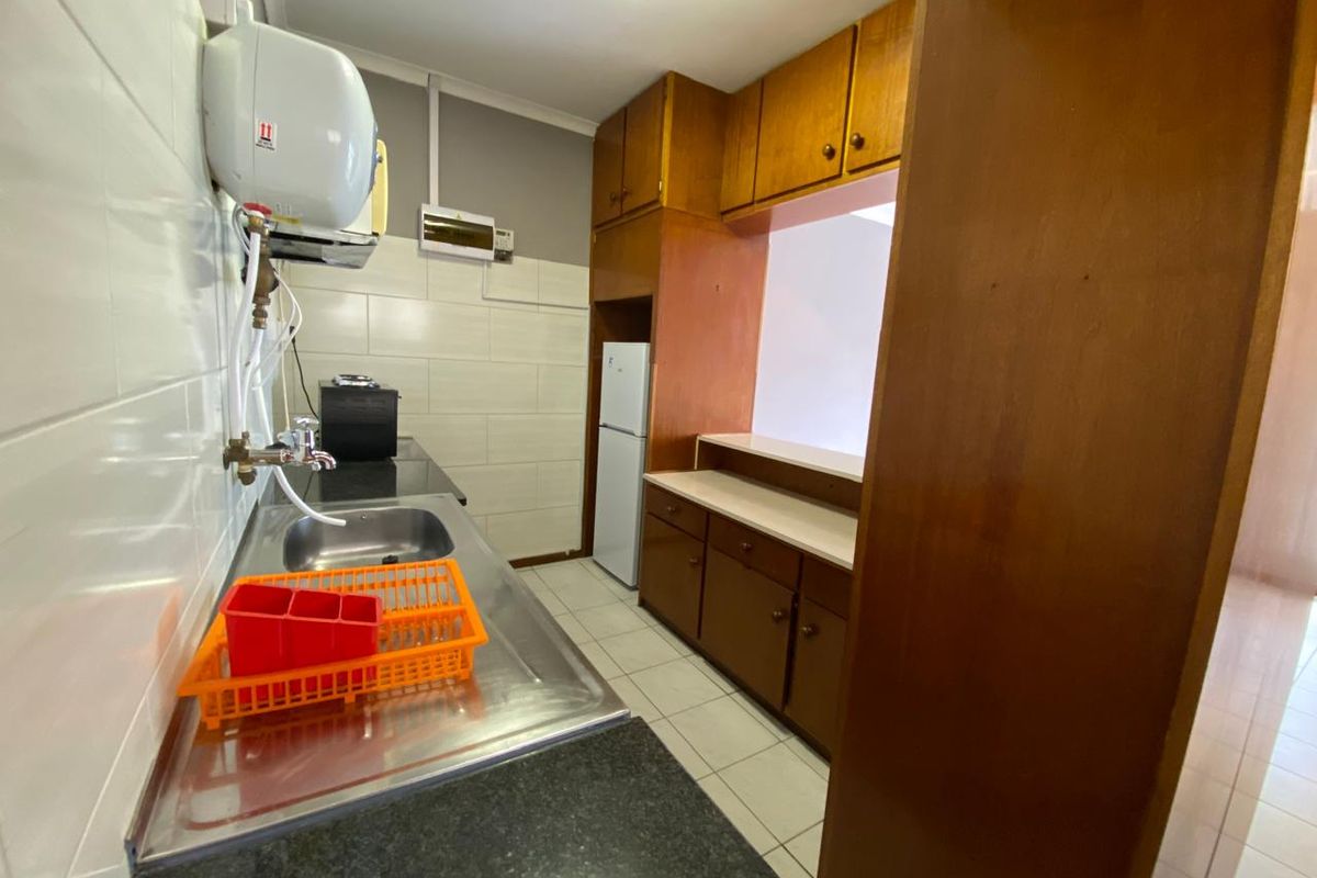 A functional kitchen featuring wooden cabinetry, tiled splashbacks, and a stainless steel sink, offering a practical layout with potential for modern updates.
