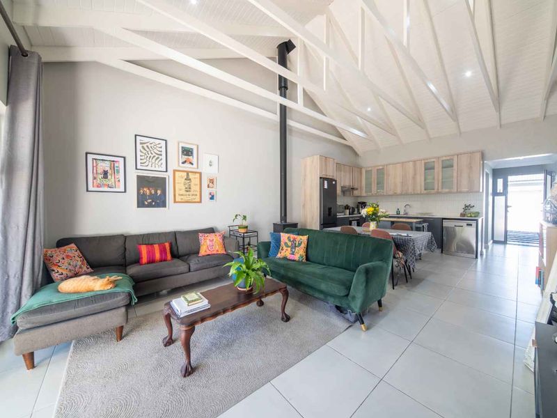 Spacious open-plan living and kitchen area featuring high vaulted ceilings with exposed trusses, a modern fireplace, and neutral tiled flooring throughout.