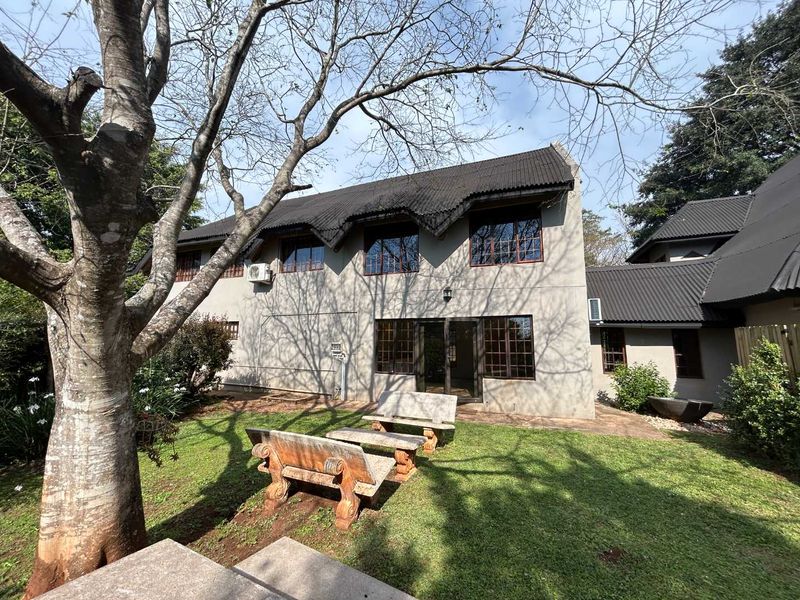 Rear view of the cottage featuring a corrugated metal roof, timber-framed windows, and a sliding glass door opening onto a private garden area.
