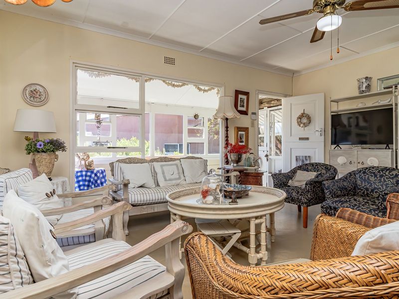 A bright and spacious living room featuring large windows, a ceiling fan, and a classic panelled ceiling, offering a comfortable and inviting atmosphere.