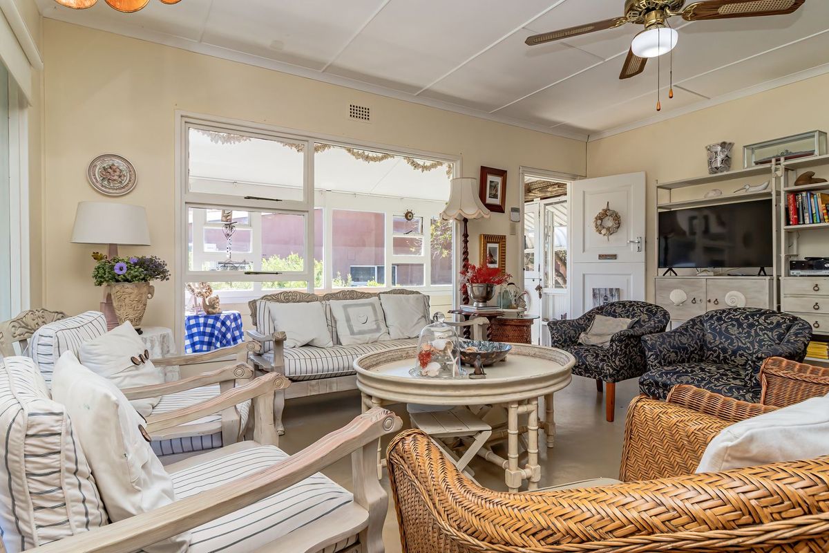 A bright and spacious living room featuring large windows, a ceiling fan, and a classic panelled ceiling, offering a comfortable and inviting atmosphere.