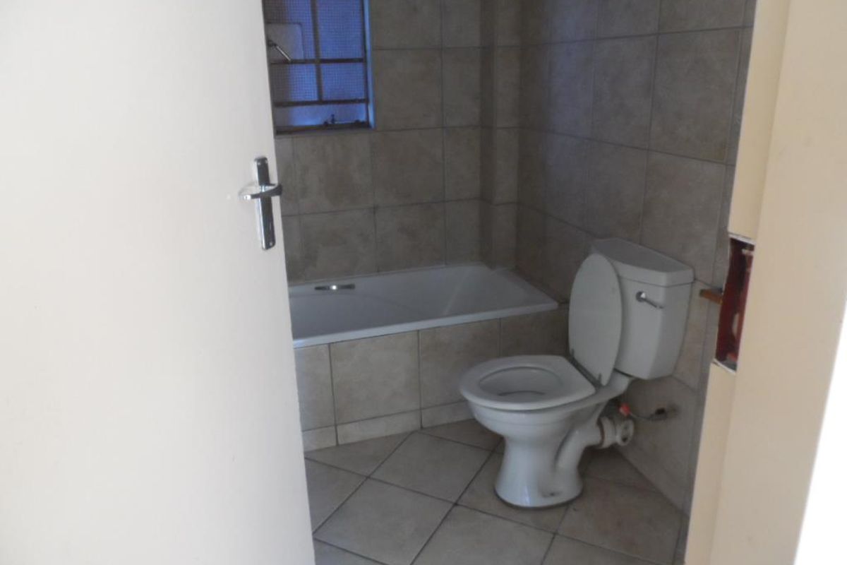 A functional bathroom featuring a built-in bathtub, ceramic wall and floor tiling, and a standard toilet suite.