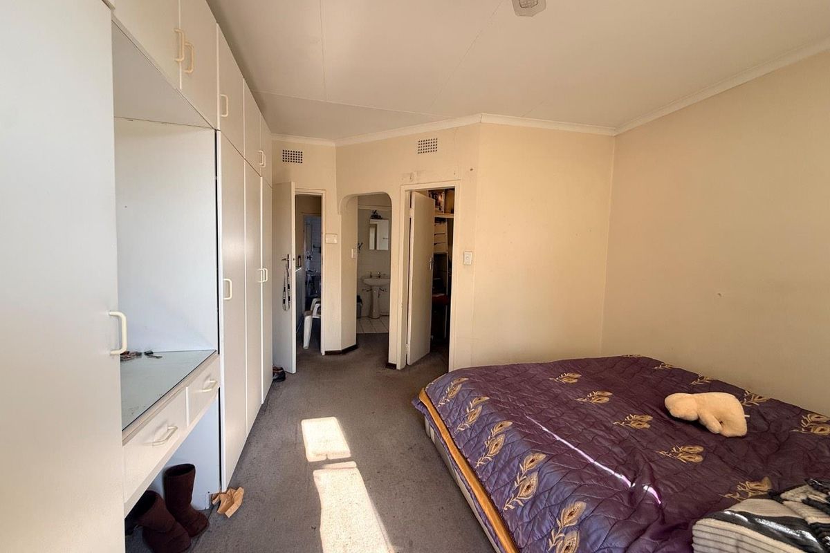 A bedroom featuring built-in cupboards, carpeted flooring, and access to an adjoining bathroom and storage area.