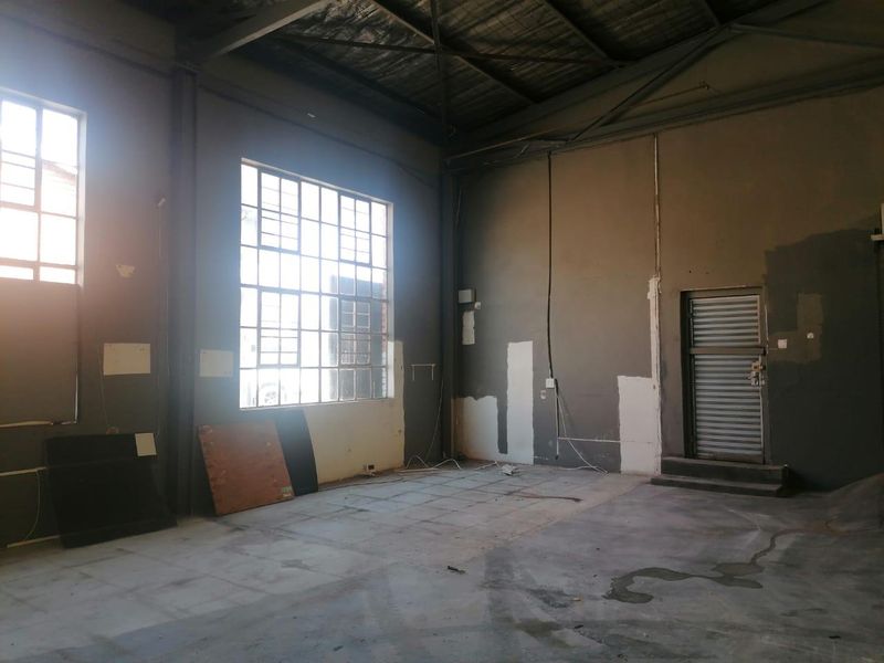 An empty industrial utility space featuring high ceilings with exposed steel trusses, large steel-framed windows, and concrete flooring, suitable for workshop or storage use.