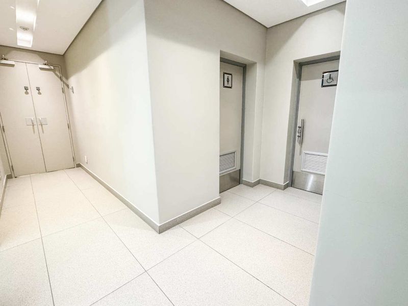 A clean, modern commercial hallway featuring tiled flooring, recessed ceiling lights, and multiple access doors including an accessible restroom entrance.
