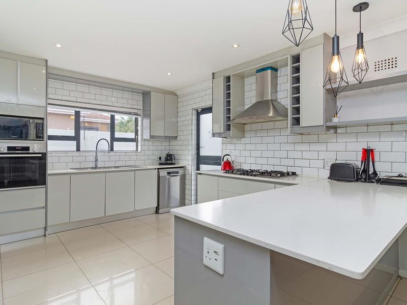 Modern kitchen featuring sleek grey cabinetry, quartz countertops, subway tile backsplash, built-in appliances, and a functional breakfast bar layout.