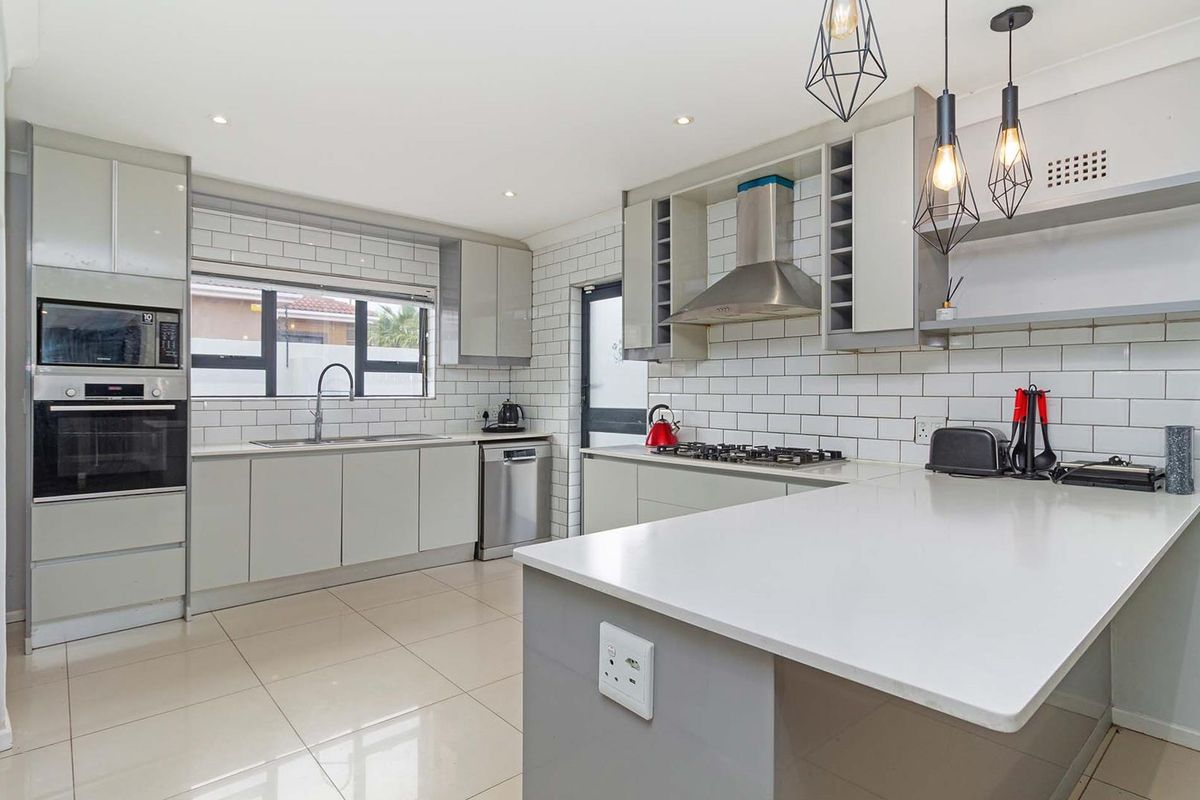 Modern kitchen featuring sleek grey cabinetry, quartz countertops, subway tile backsplash, built-in appliances, and a functional breakfast bar layout.