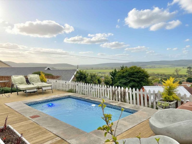 Outdoor pool area featuring timber decking, stone coping, and a picket fence, set against a scenic landscape view.