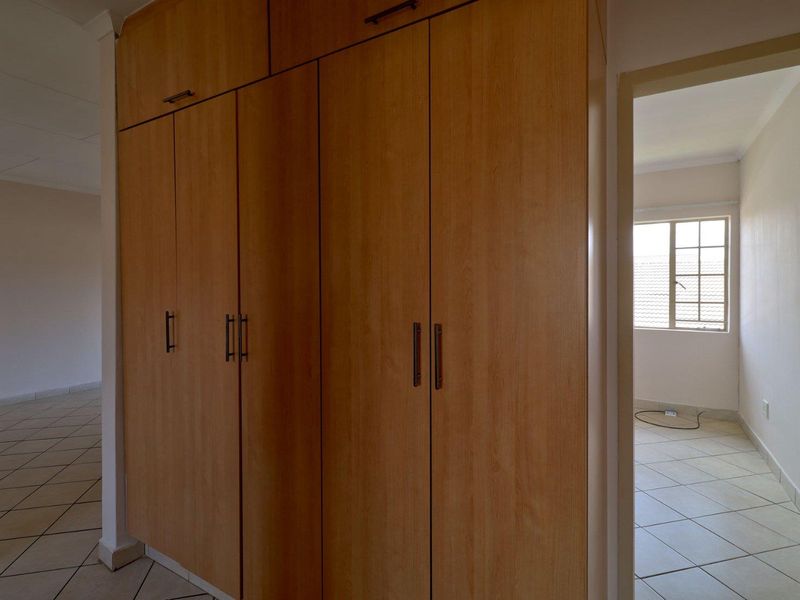 A bright, empty bedroom featuring built-in wooden cupboards and neutral tiled flooring, offering a clean and versatile space.