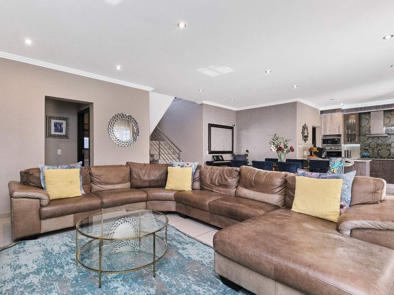 Spacious open-plan living area featuring a modern kitchen with built-in appliances, tiled flooring, recessed lighting, and an integrated staircase.