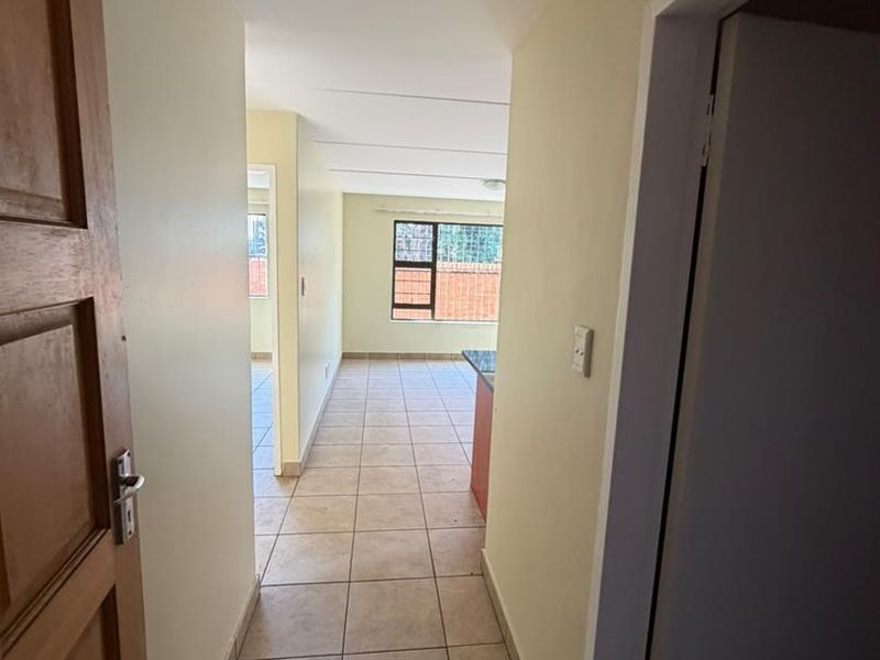 A view through a tiled hallway leading into an open plan living area with natural light and neutral wall finishes.
