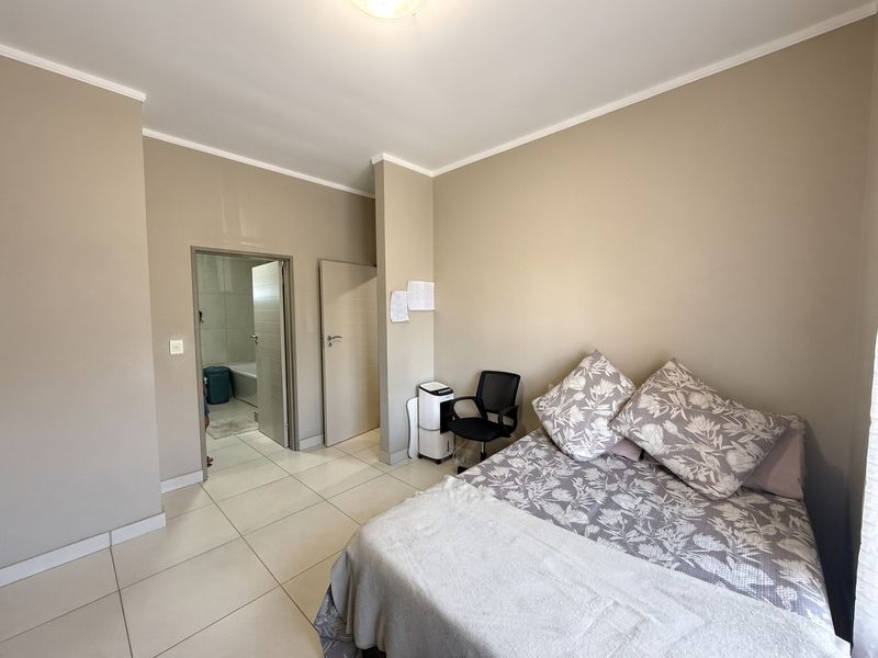 A well-maintained bedroom featuring neutral wall tones, large format floor tiles, and direct access to an en-suite bathroom.