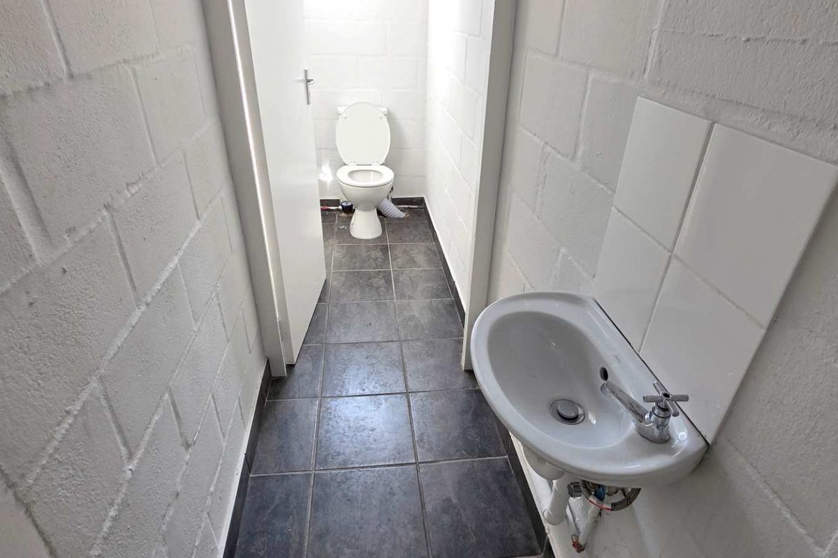 A functional industrial-style restroom featuring a wall-mounted basin, tiled flooring, and a private toilet cubicle with exposed blockwork walls.