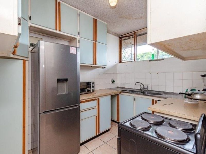 A compact kitchen featuring dated cabinetry, laminate countertops, a double sink, and tiled flooring, offering potential for a modern renovation.