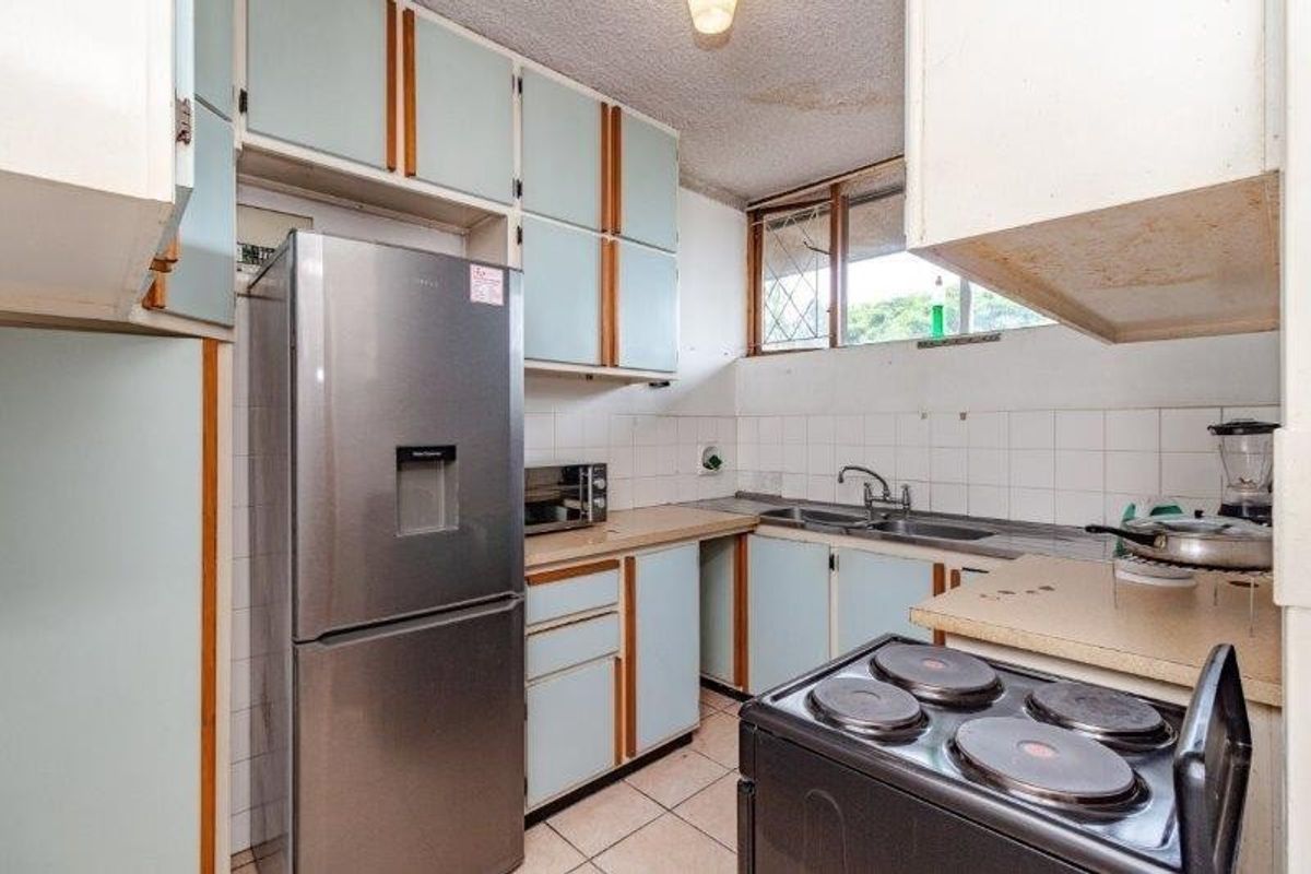 A compact kitchen featuring dated cabinetry, laminate countertops, a double sink, and tiled flooring, offering potential for a modern renovation.