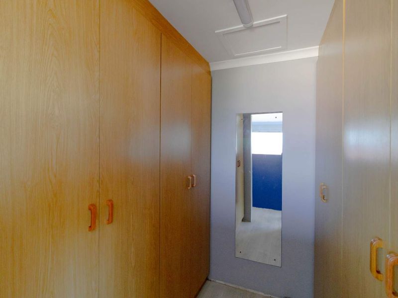 A narrow hallway featuring extensive built-in wooden cabinetry and a ceiling access hatch, providing ample storage space.