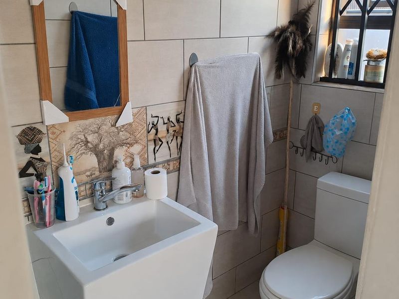 A compact bathroom featuring a modern pedestal basin, chrome mixer tap, and tiled walls with decorative accents, including a toilet and security-fitted window.