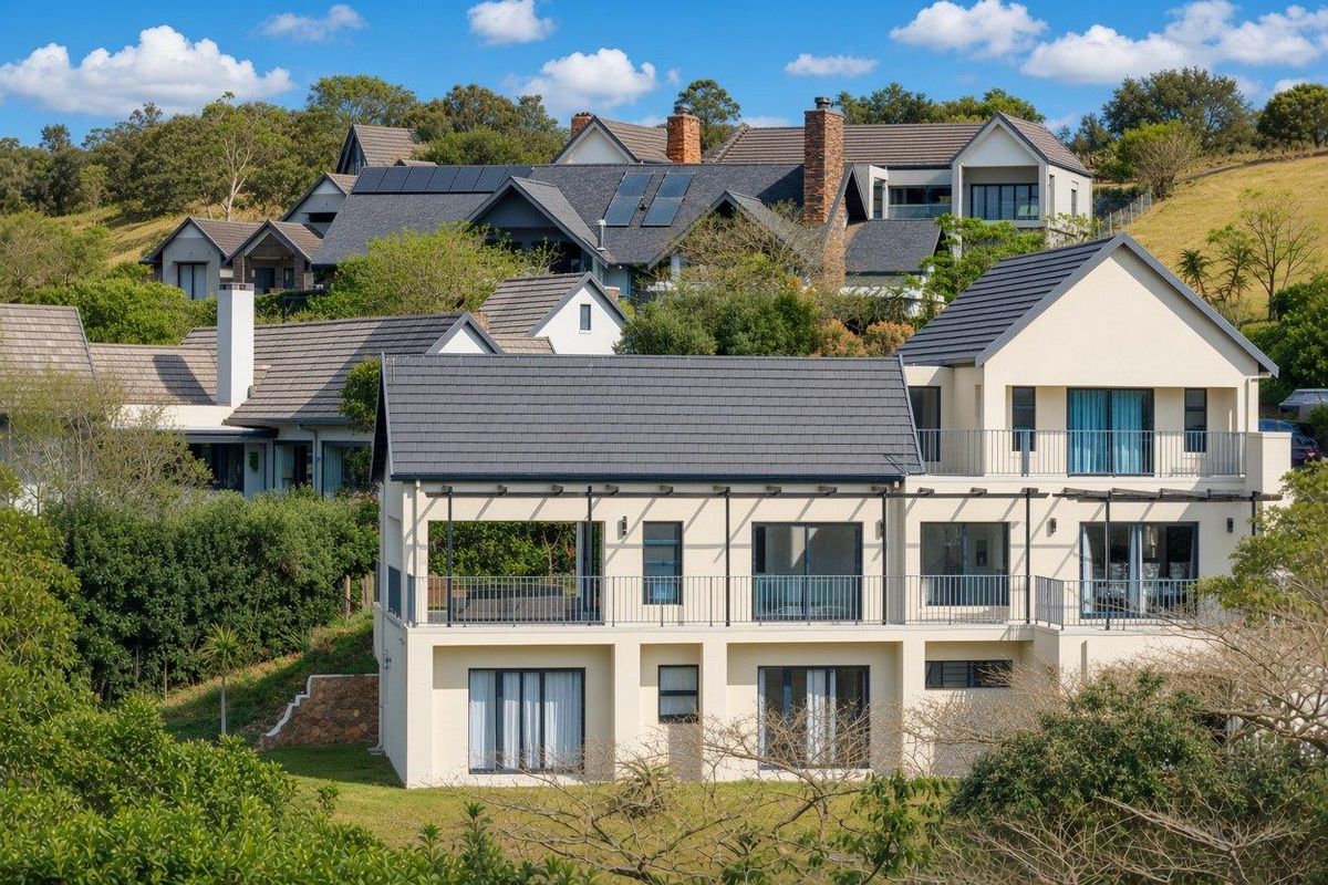 A multi-level residential property featuring a tiled roof, solar panels, and spacious balconies with metal railings, set within a landscaped estate environment.