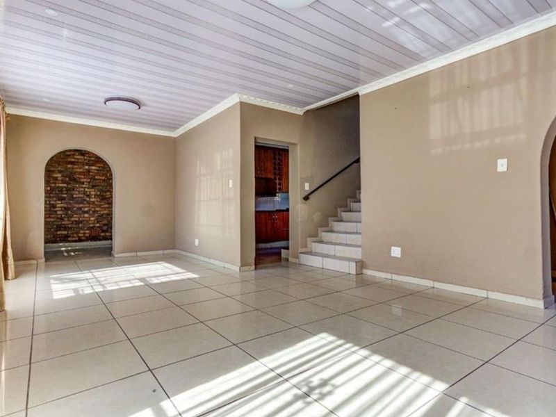Spacious open-plan living area featuring tiled floors, a staircase, and a unique arched brick feature wall, offering a blank canvas for modern updates.