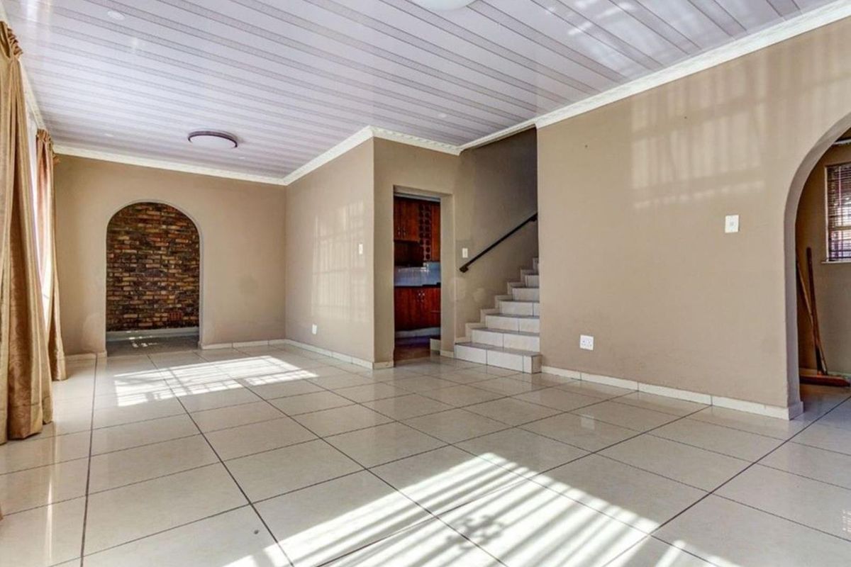 Spacious open-plan living area featuring tiled floors, a staircase, and a unique arched brick feature wall, offering a blank canvas for modern updates.