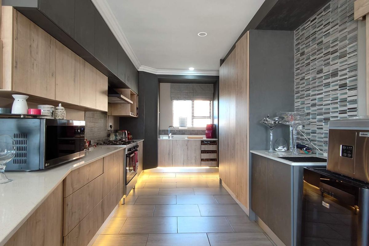 Modern galley-style kitchen featuring two-tone cabinetry, stone countertops, integrated appliances, mosaic tile backsplash, and ambient under-cabinet lighting.