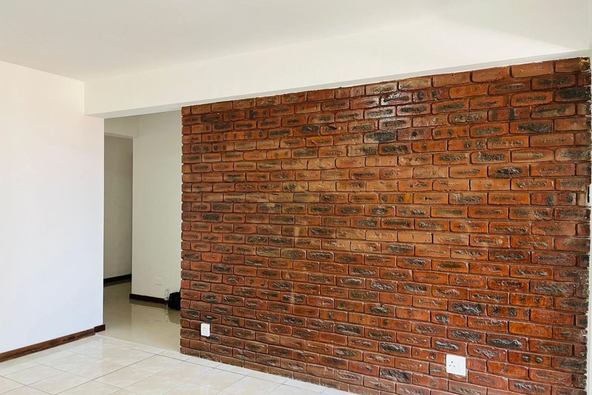 A bright, empty living area featuring a prominent exposed brick feature wall and neutral tiled flooring, offering a clean canvas for interior design.
