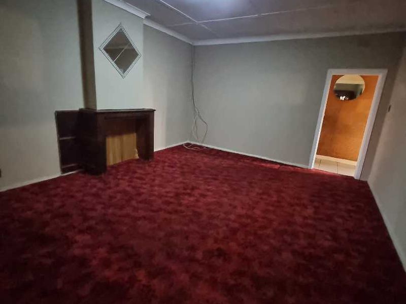 An empty living room featuring a fireplace, red carpet flooring, and neutral wall finishes, offering a blank canvas for renovation.