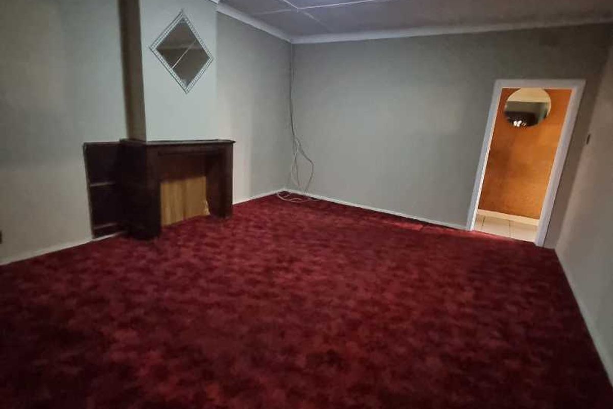 An empty living room featuring a fireplace, red carpet flooring, and neutral wall finishes, offering a blank canvas for renovation.