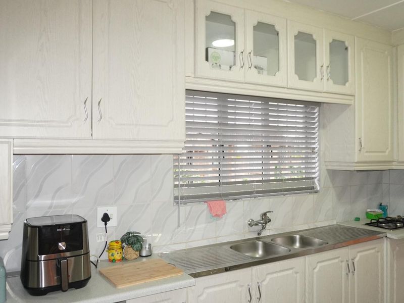 A functional kitchen featuring white cabinetry, a double bowl stainless steel sink, tiled splashbacks, and a built-in gas hob with venetian blinds.