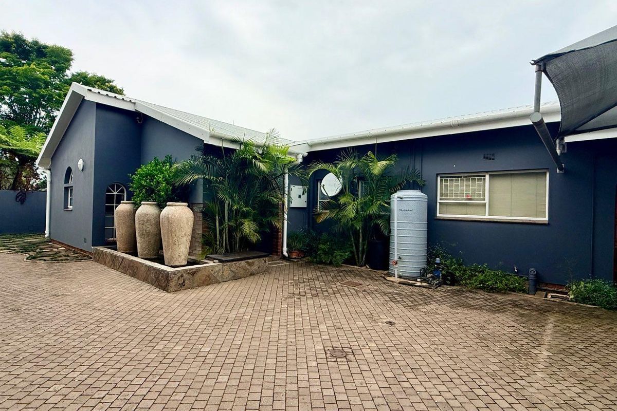 Exterior view of the property featuring a paved driveway, stone-clad planter box, and a water storage tank against a dark-painted facade.