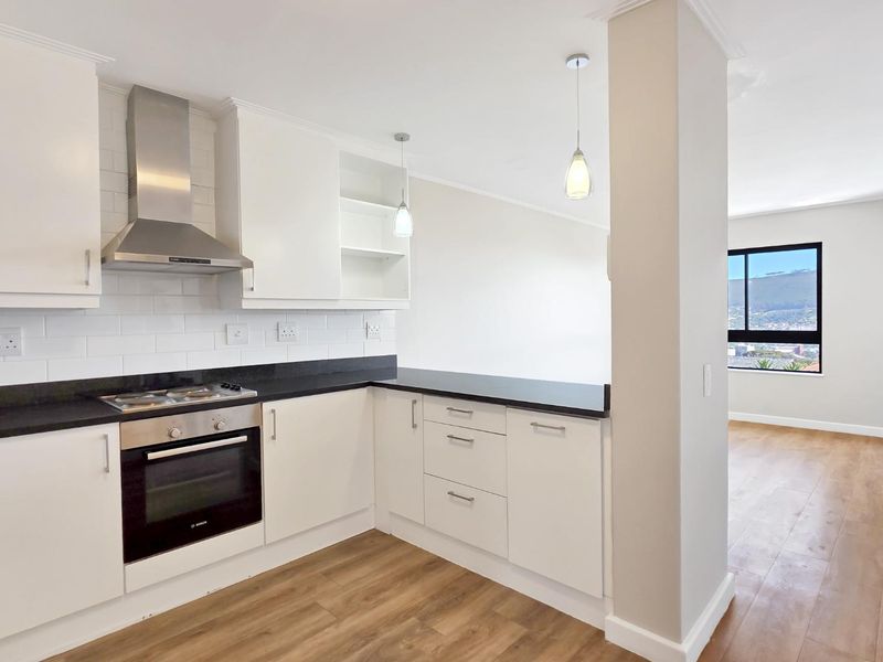 Modern open-plan kitchen featuring white cabinetry, black granite countertops, stainless steel appliances, and subway tile backsplash, flowing into a bright living area.