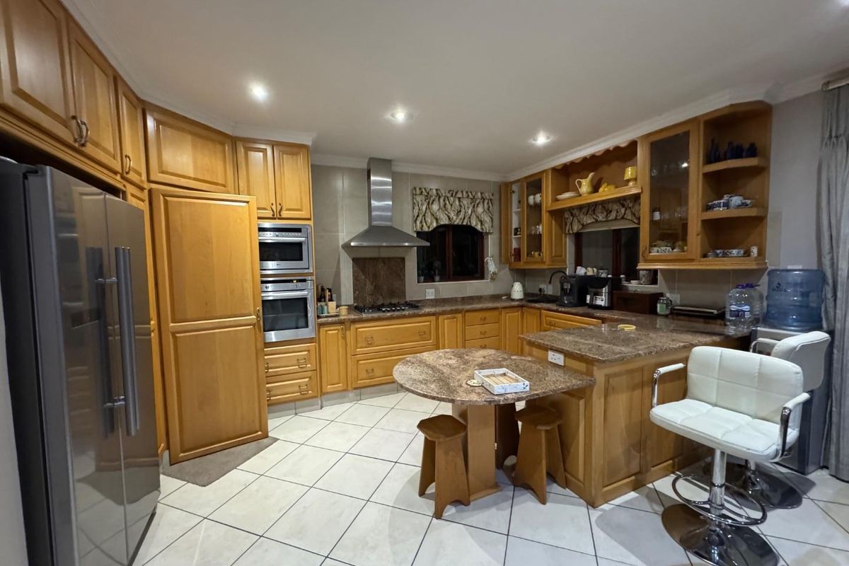 A spacious kitchen featuring wooden cabinetry, granite countertops, a built-in oven and microwave, stainless steel extractor fan, and tiled flooring.