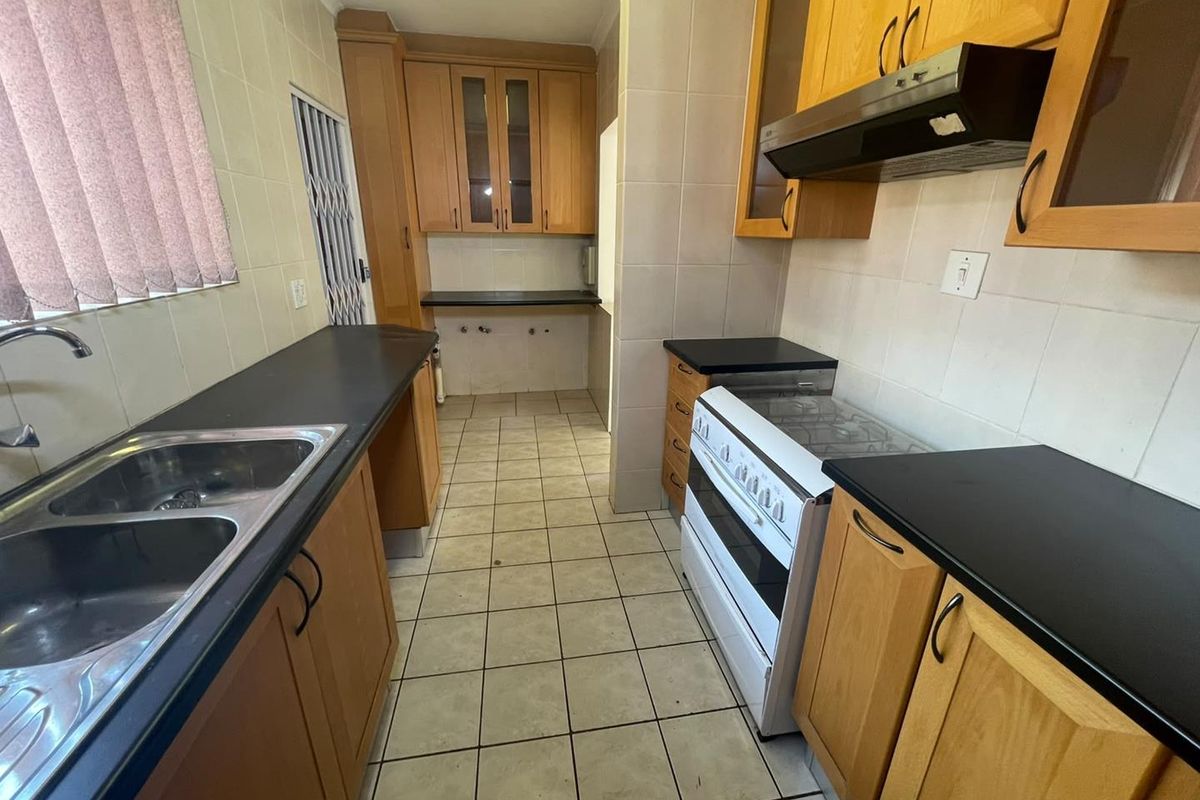 A functional kitchen featuring wooden cabinetry, dark laminate countertops, a freestanding stove with extractor fan, and tiled flooring throughout.
