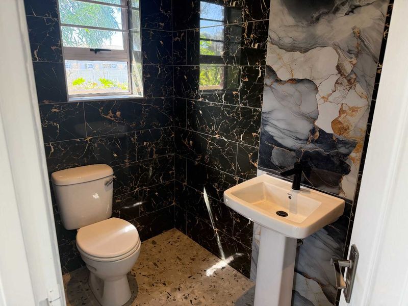 A modern, compact bathroom featuring striking black marble-effect wall tiles, a feature accent wall, pedestal basin, and terrazzo-style flooring.
