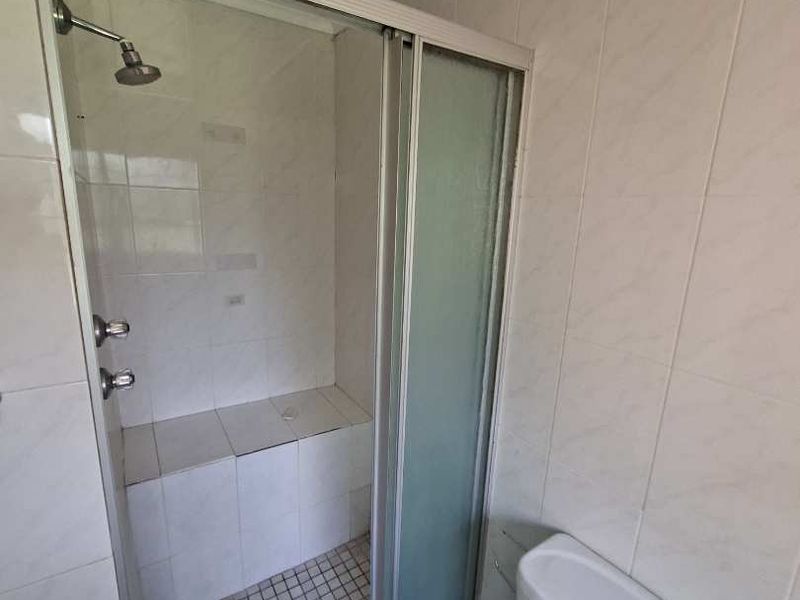 A functional bathroom featuring a tiled shower enclosure with a built-in bench and a standard toilet.