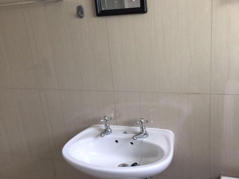 A functional bathroom featuring a white pedestal basin with chrome taps and neutral wall tiling.