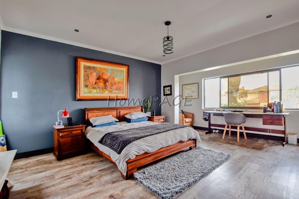 Spacious bedroom featuring laminate flooring, a feature wall, and a built-in desk area with large windows providing natural light.
