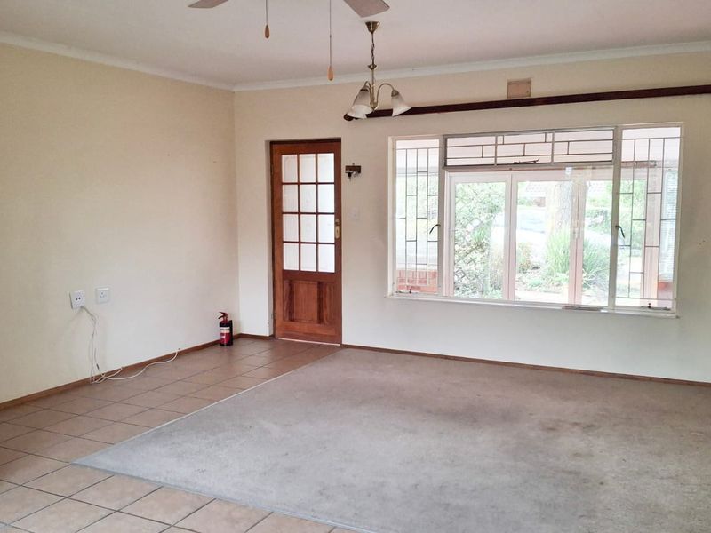 An empty living room featuring a combination of tiled and carpeted flooring, a timber door, and large windows with security bars.